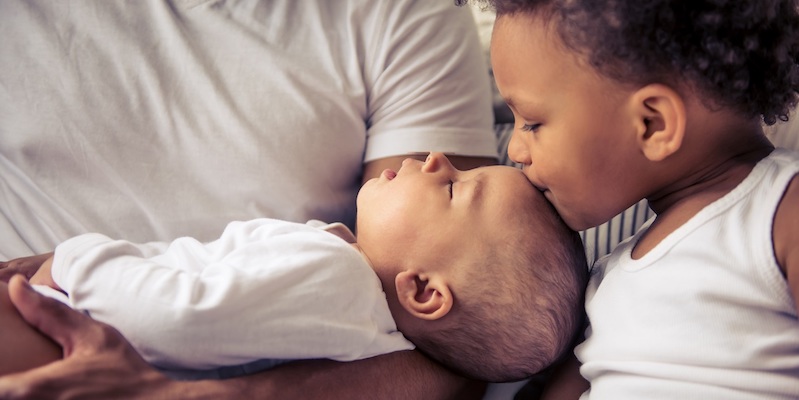 Little baby is sleeping in dad's arms while her sister is kissing her