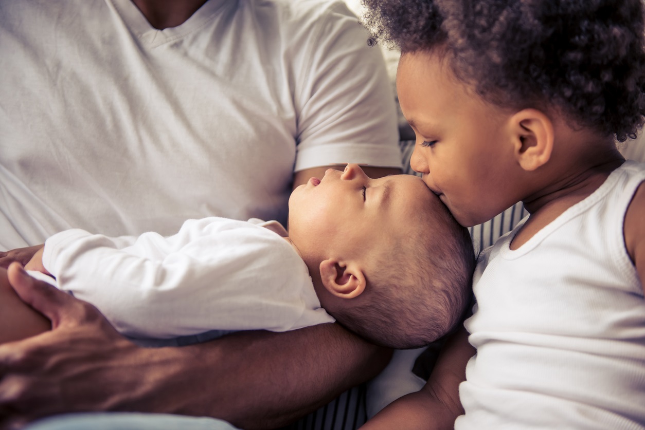 A young boy kissing the forehead of an infant being held by an adult