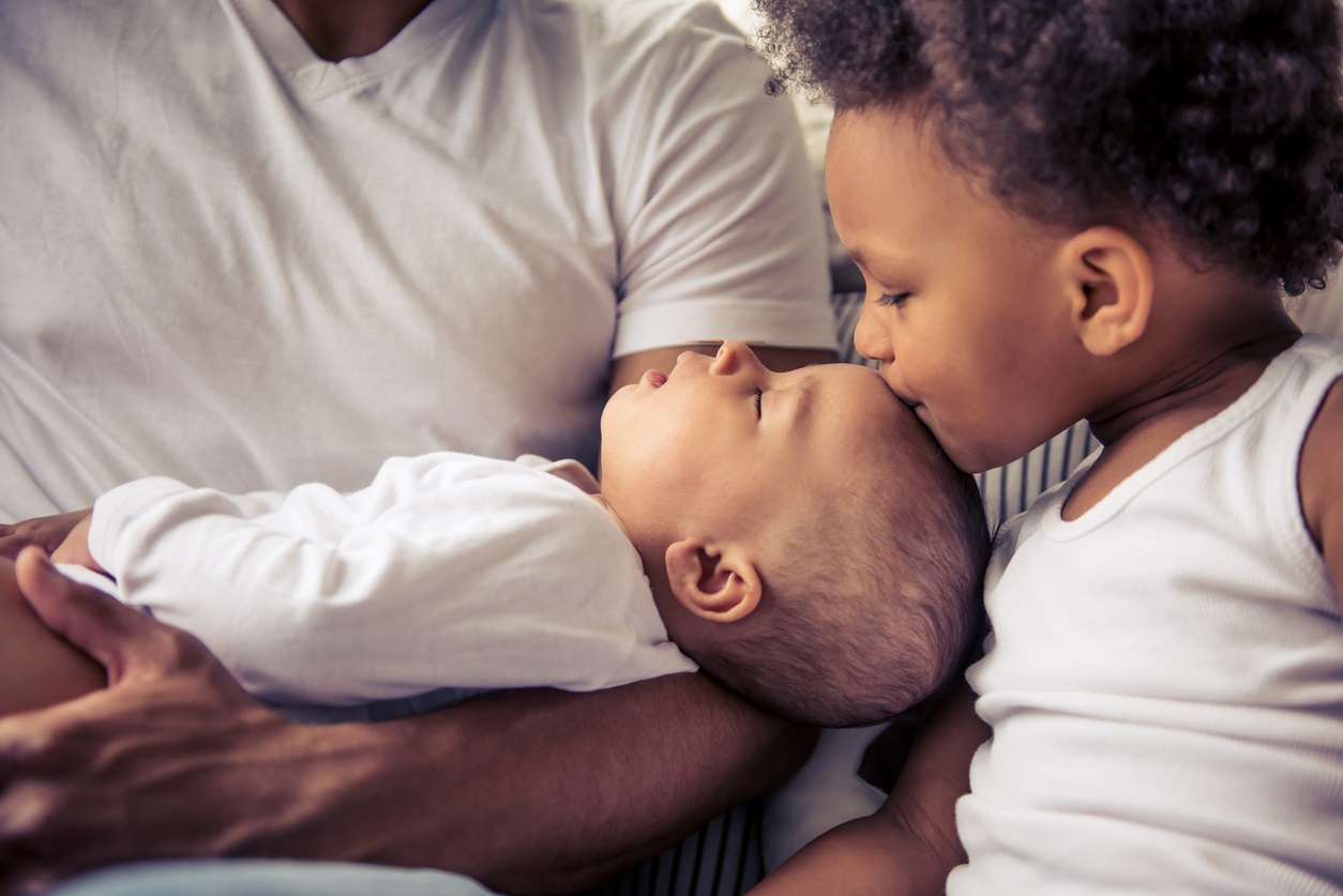 A young boy kissing the forehead of an infant being held by 