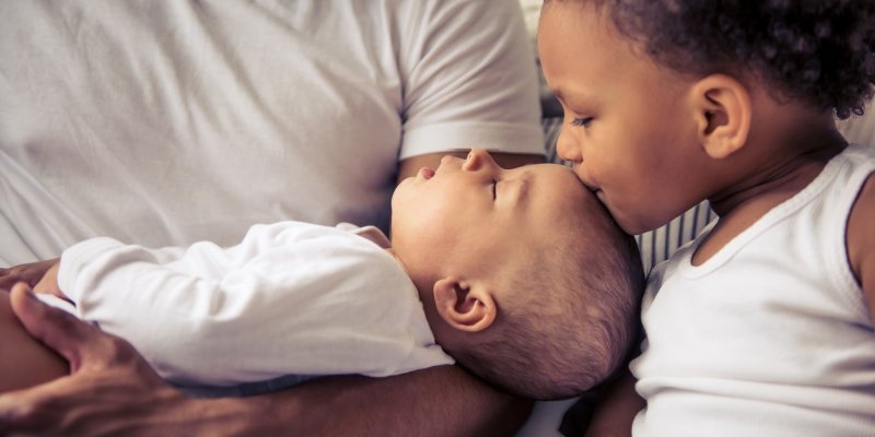 A young boy kissing the forehead of an infant being held by 
